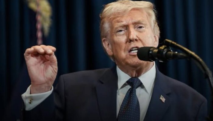 Donald Trump falando em um microfone com a mão esquerda levantada e gesticulando