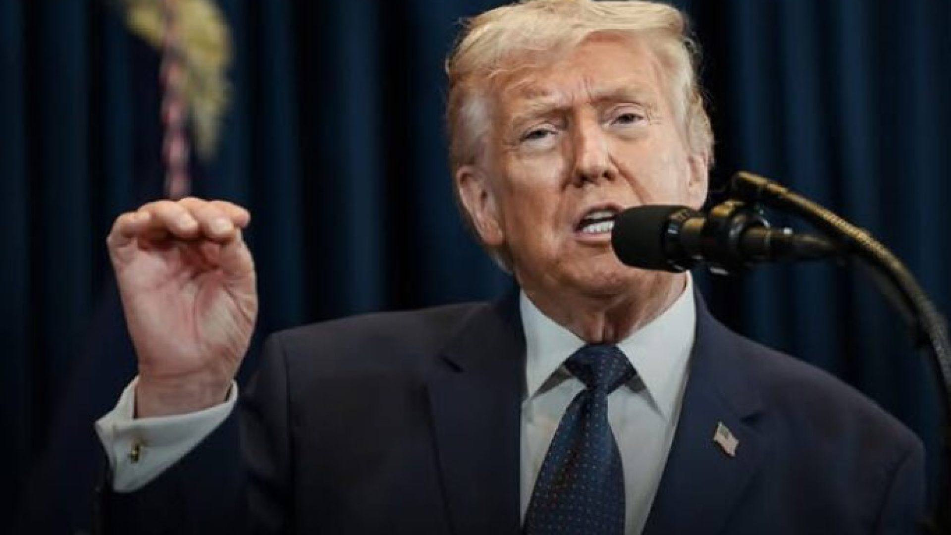 Donald Trump falando em um microfone com a mão esquerda levantada e gesticulando