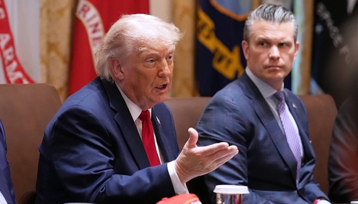 Veículos passam diante de um cartaz com um gráfico do estreito de Ormuz e os lábios cosidos do presidente dos EUA, Donald Trump, numa praça no centro de Teerão, Irão, sábado, 2 de