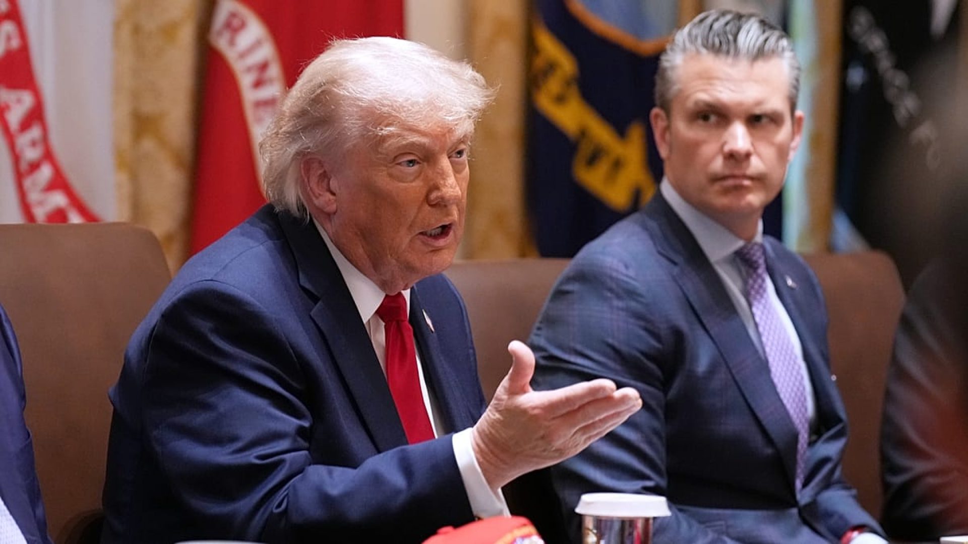 Veículos passam diante de um cartaz com um gráfico do estreito de Ormuz e os lábios cosidos do presidente dos EUA, Donald Trump, numa praça no centro de Teerão, Irão, sábado, 2 de